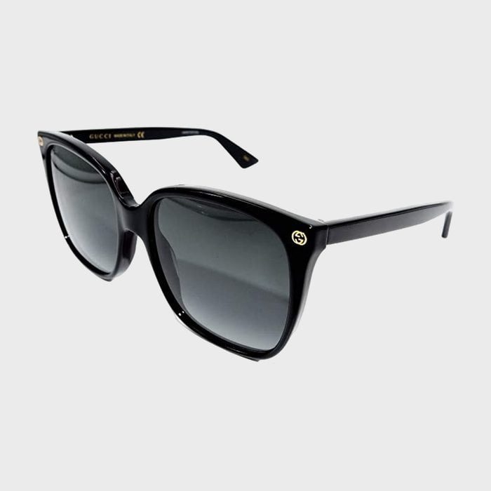 Black sunglasses resting on a white surface, featuring dark lenses and small gold branding on the frame sides.