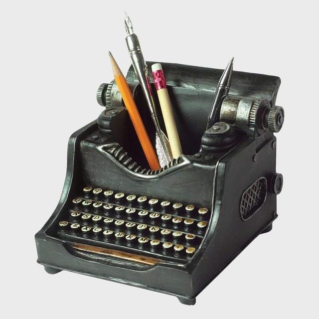 A black typewriter-shaped container holds pens and pencils, set against a plain background.