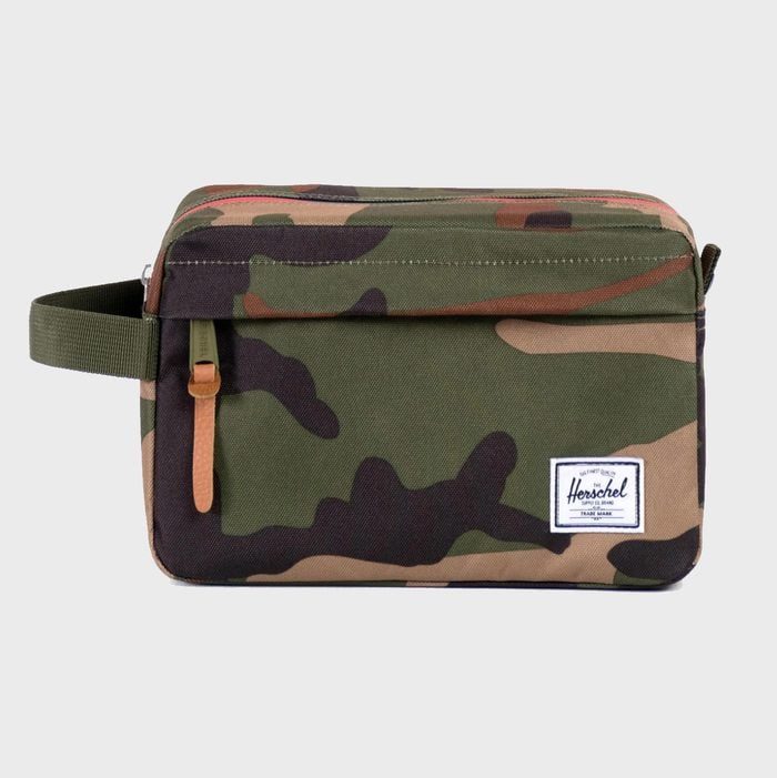 Camouflage toiletry bag with a zipper and side handle, featuring a small white label, positioned against a plain gray background.