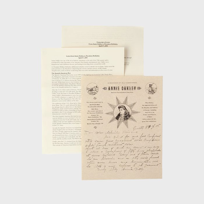 Documents lie on a flat surface, featuring handwritten letters and printed text. The main page highlights 