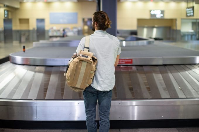 young man stands alone waiting for luggage by empty baggage carousel.