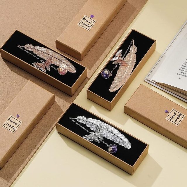 Feather-shaped metal bookmarks rest in black-lined boxes labeled 