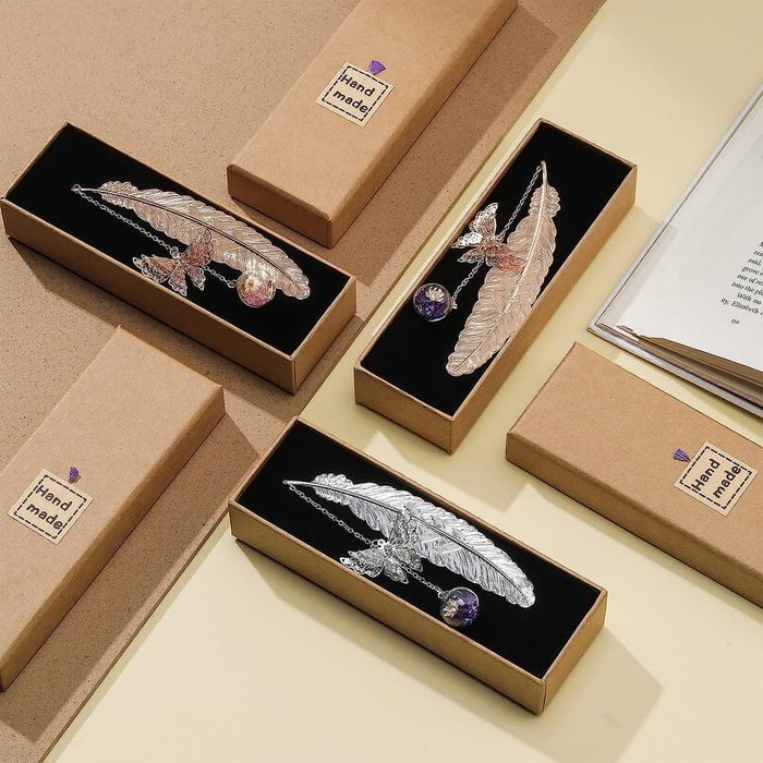 Feather-shaped metal bookmarks rest in black-lined boxes labeled 