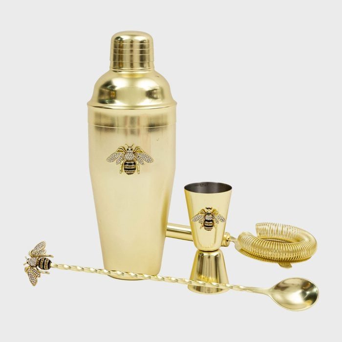 Gold cocktail set featuring a shaker, jigger, stirring spoon, and strainer, adorned with bee motifs, displayed against a plain background.