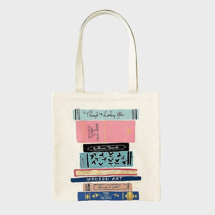 Tote bag displays an illustration of colorful stacked books, featuring titles like 