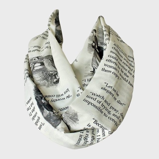 A white scarf displays printed text and illustrations, resembling pages from a book, elegantly folded against a plain backdrop.