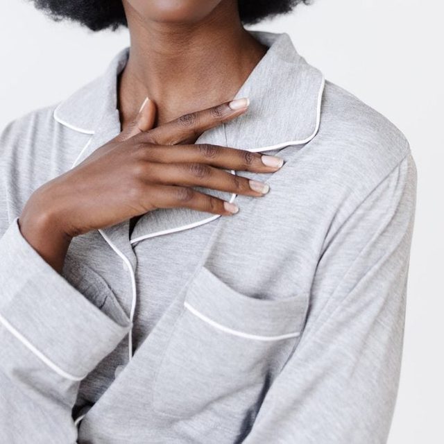 A hand rests on a gray, collared pajama top with white piping, set against a plain background.