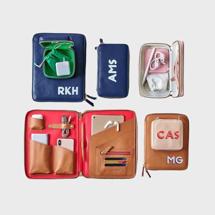 Organizers hold electronic accessories; various colors; initials RKH, AMS, CAS, MG on covers; compartments for chargers, cables, and devices; set on plain background.