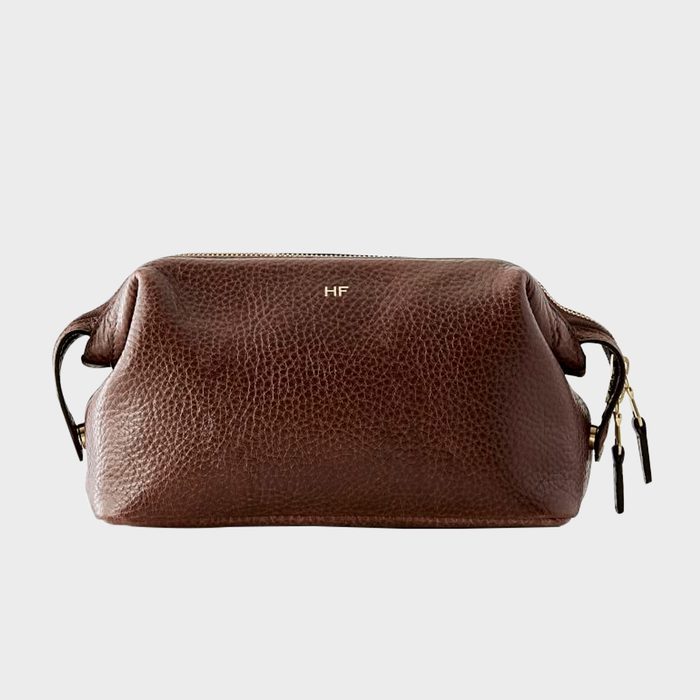 Brown leather pouch resting with zipped top, initials 