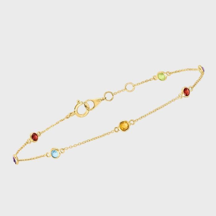 Gold bracelet features colorful gemstones evenly spaced, resting on a plain white background.