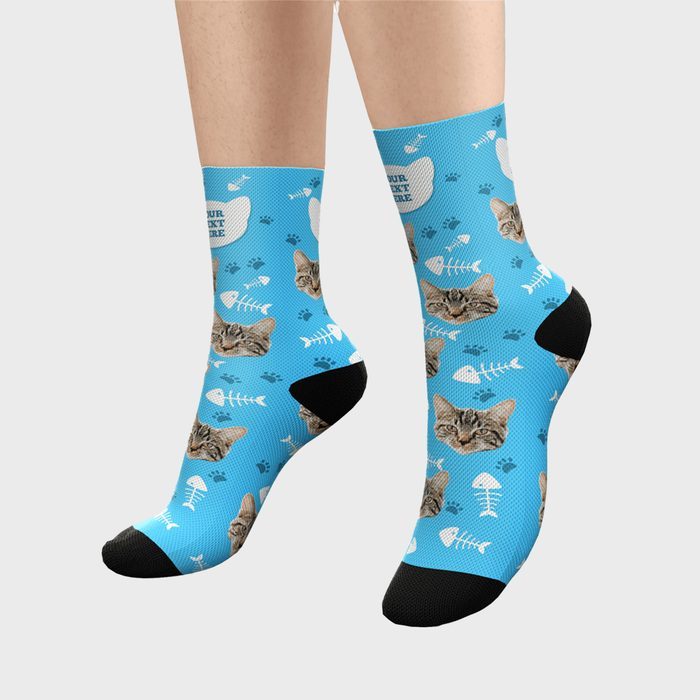 Blue socks display cat faces and fish bones, worn on feet with black toes and heels.
