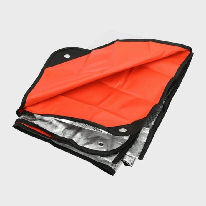 A folded orange and silver tarp partially unfurls, revealing multiple layers and grommets, set against a plain, light background.