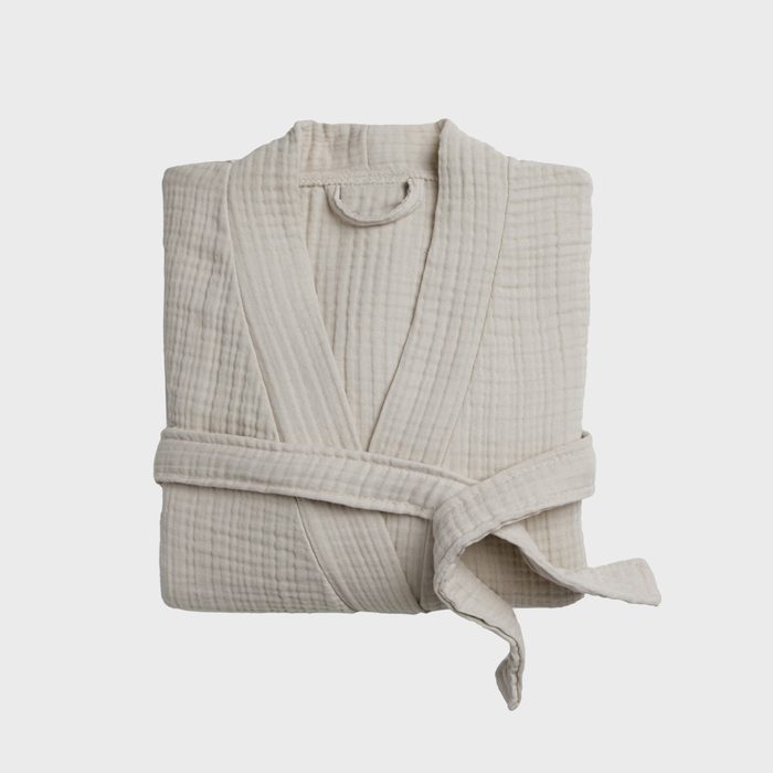 A folded beige bathrobe lies neatly with its belt tied, set against a plain white background.