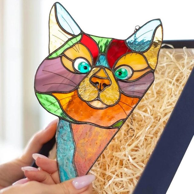 Stained glass cat, being held, surrounded by packaging straw in a box.
