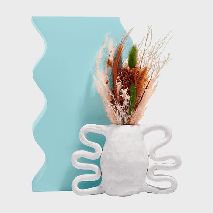 Sculptural vase holds dried flowers against teal geometric backdrop, creating a modern artistic display.