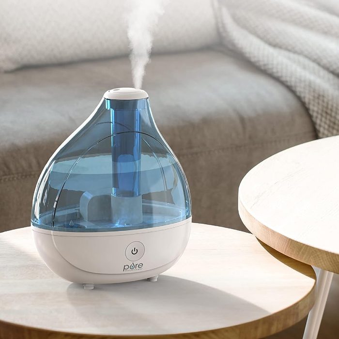 Humidifier releasing mist on a wooden table in a cozy living room setting.