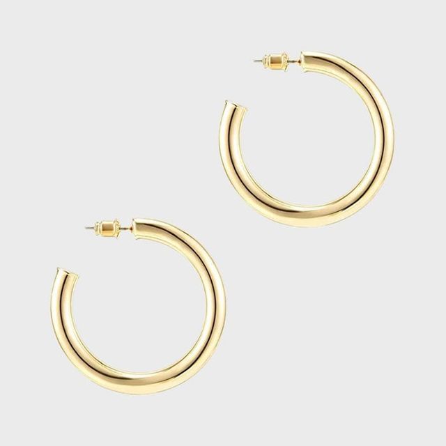 Gold hoop earrings lie on a plain, light background, gleaming under soft lighting.