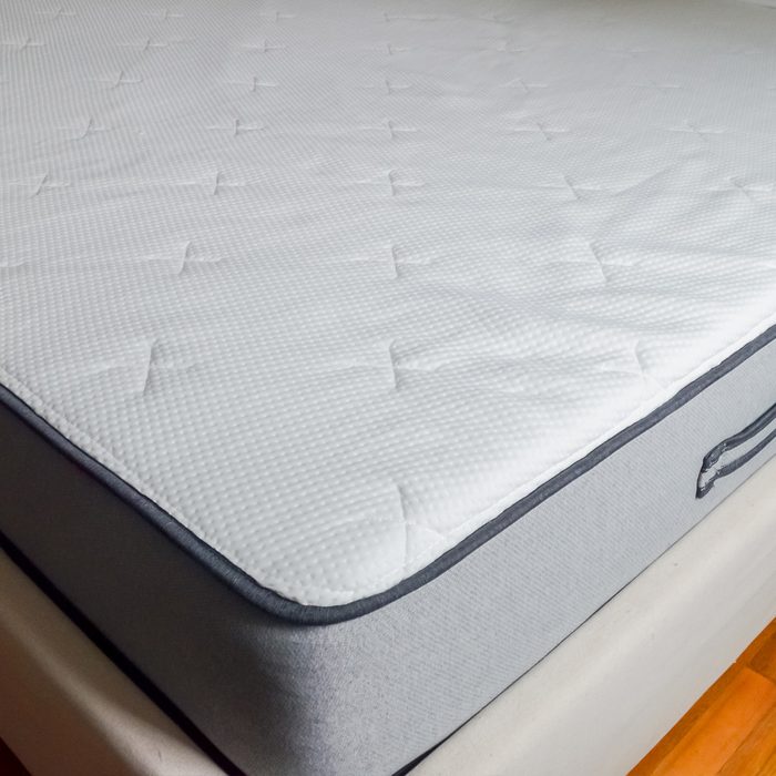 A white mattress rests neatly on a bed frame, appearing firm and clean, with a textured, quilted pattern on its surface.