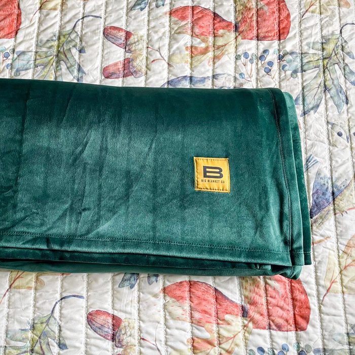 Green blanket lies folded on a floral quilted bedspread. A small yellow label reads 