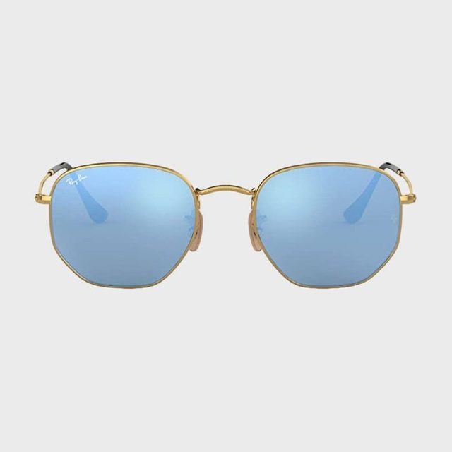 Gold-framed sunglasses reflect blue-tinted lenses, set against a plain gray background. The word 