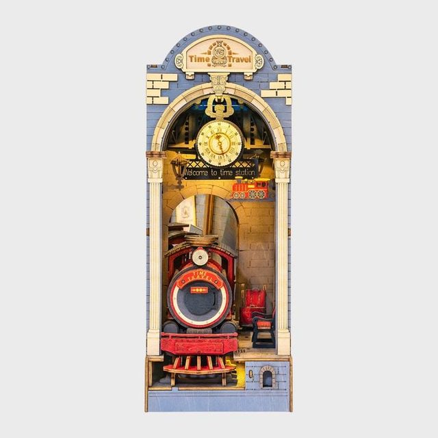 Train emerges from a stone archway under a clock; sign reads 