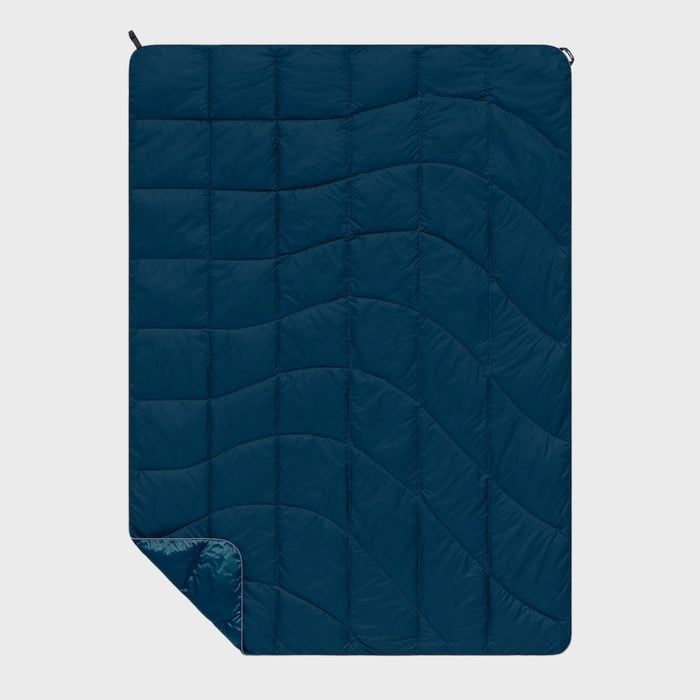 A blue quilted blanket lies flat, featuring wave-like stitching patterns and a corner folded over, set against a plain white background.