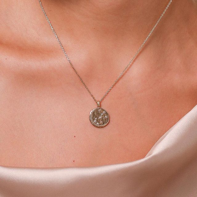 Necklace displays round pendant resting on a bare collarbone against a smooth, light-colored fabric backdrop.