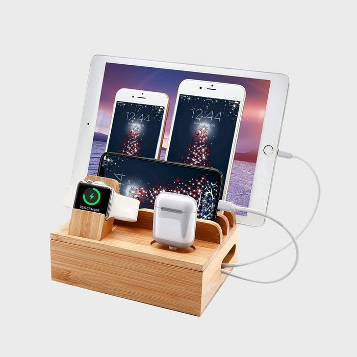 Wooden docking station holds a smartwatch, smartphone, tablets, and wireless earphones; devices are charging amidst a neat technology setup.