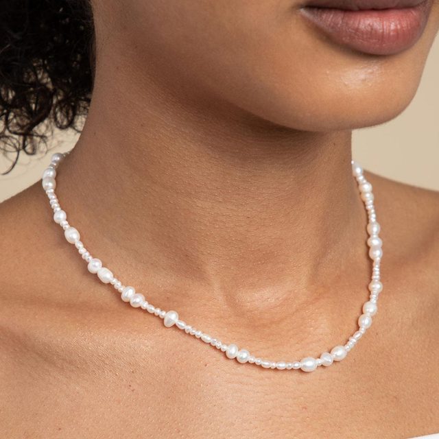 Pearl necklace adorns a neck, with varying pearl sizes, set against a neutral background.