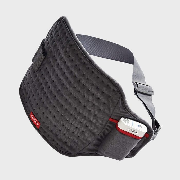 A padded, textured belt rests with attached control device; designed for comfort, featuring adjustable straps. Gray background, Sunbeam branding on the belt.