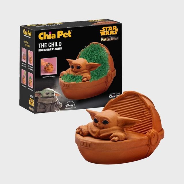 Planter shaped like a small creature sits surrounded by green sprouts; packaging in the background displays the product and related branding.