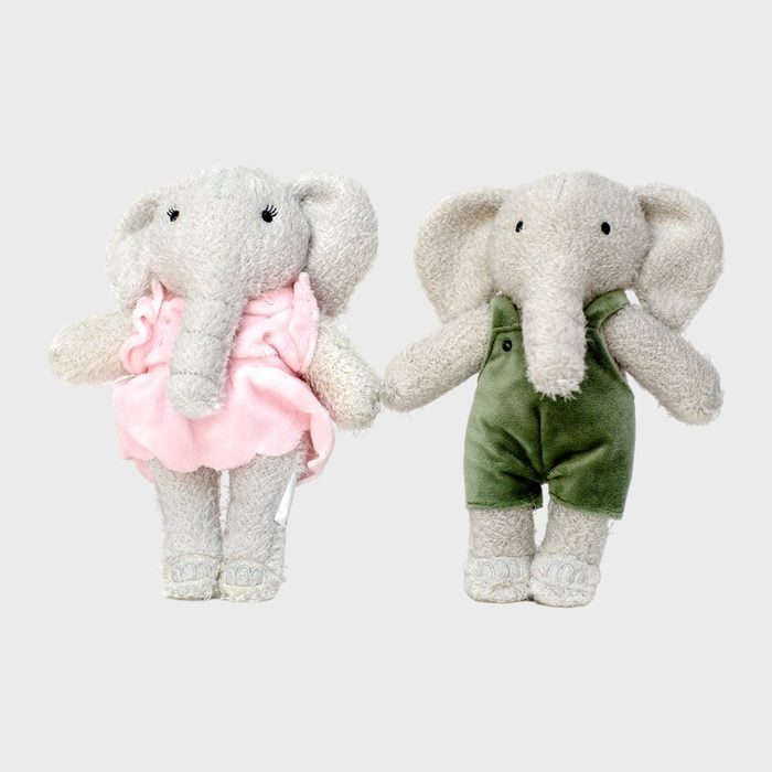 Two plush elephants stand side by side; one wears a pink dress, the other a green outfit, against a plain background.
