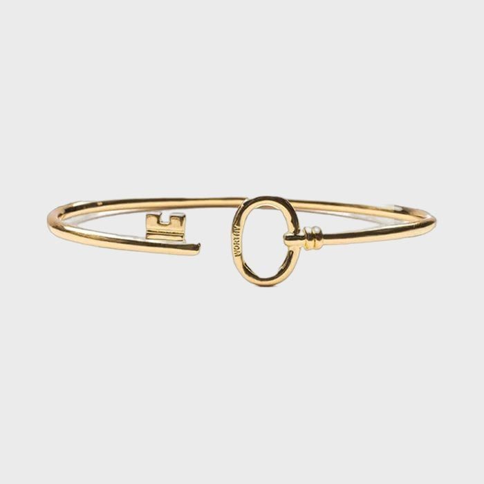 A gold bracelet shaped as a key is displayed on a plain white background. Text 