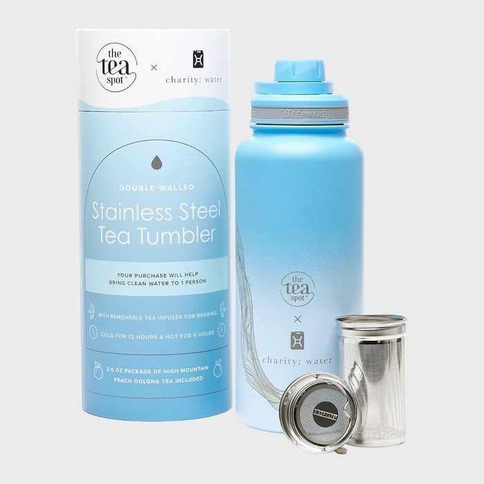 Tumbler set includes a blue stainless steel tea tumbler with infuser and cylindrical packaging, promoting Charity: Water collaboration in a minimalist setting.