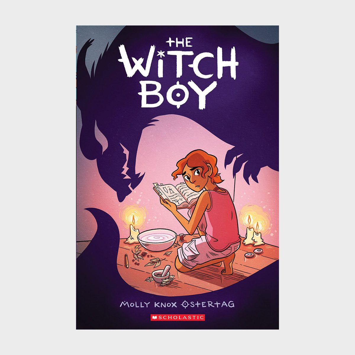 A boy reads a book, surrounded by magical items and candles, with a shadowy creature looming in the background. Text reads "The Witch Boy."
