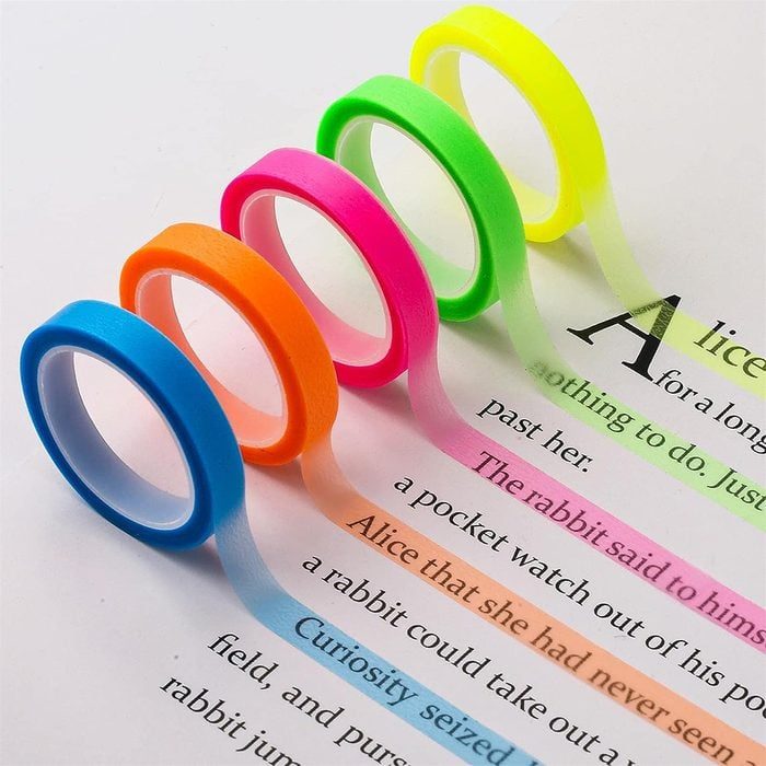 Colored tape rolls highlighting book text, running in parallel lines: blue, orange, pink, green, and yellow, enhancing specific words.