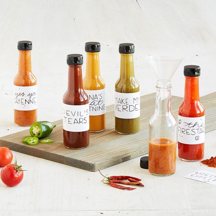 Bottles labeled with hot sauce names stand on a wooden board, surrounded by sliced jalapeÃ±os, tomatoes, and chili peppers, illustrating a spicy theme.