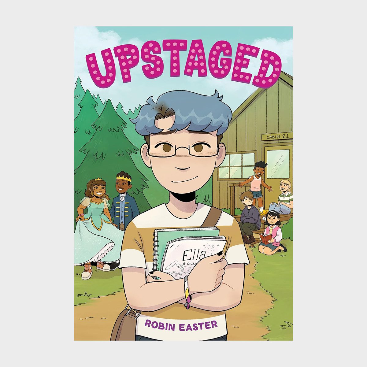 Person holding notebook standing confidently in front of a cabin, surrounded by children in costumes and trees. Text: "UPSTAGED," "Ella," "ROBIN EASTER."