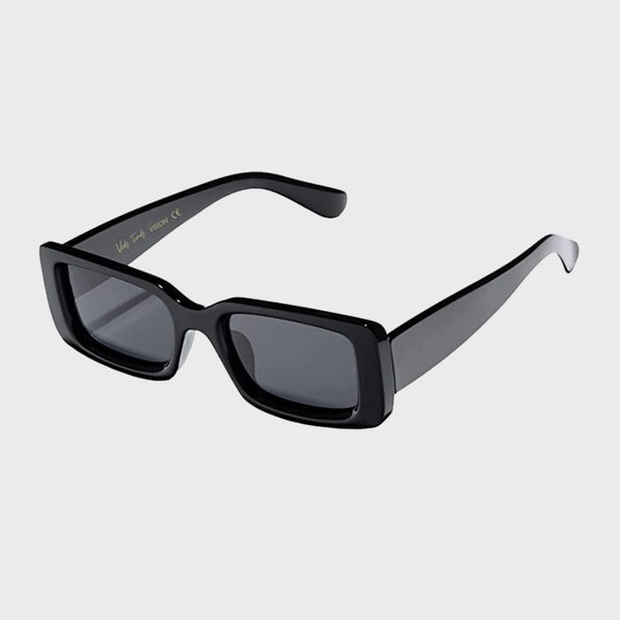 Sunglasses rest on a plain surface; thick black frames and dark lenses contrast against the light gray background.