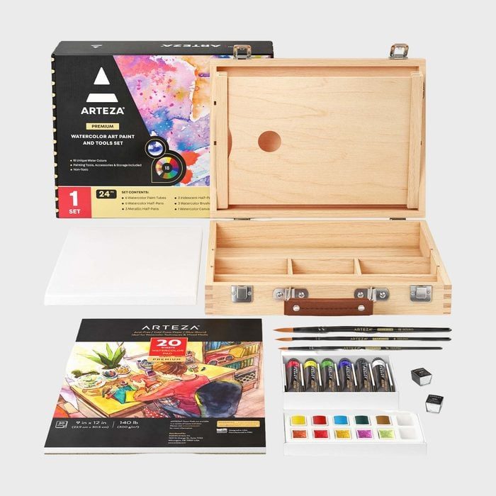 Wooden art kit sits open, displaying brushes, paints, and canvases, surrounded by packaging with vibrant designs in a studio setting.