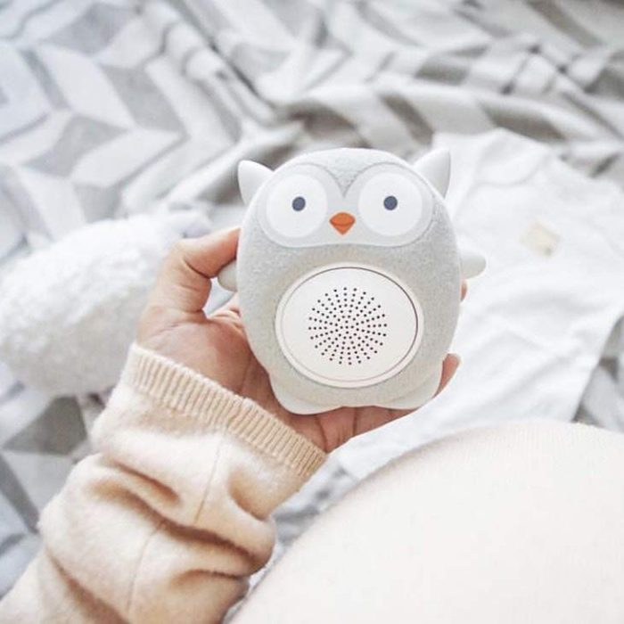 A hand holds a plush owl-shaped speaker against a soft, textured fabric surface.