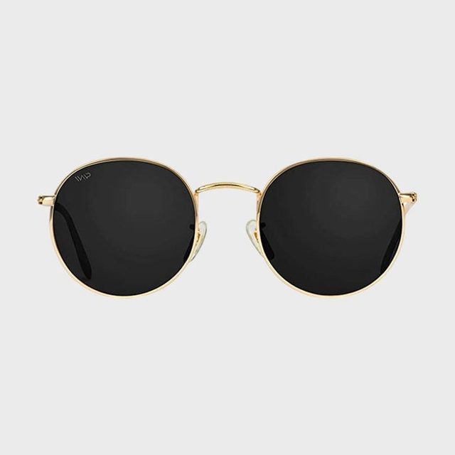 Round sunglasses with black lenses rest against a plain gray background, featuring a thin gold frame.