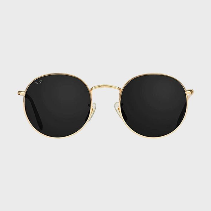 Round sunglasses with black lenses rest against a plain gray background, featuring a thin gold frame.