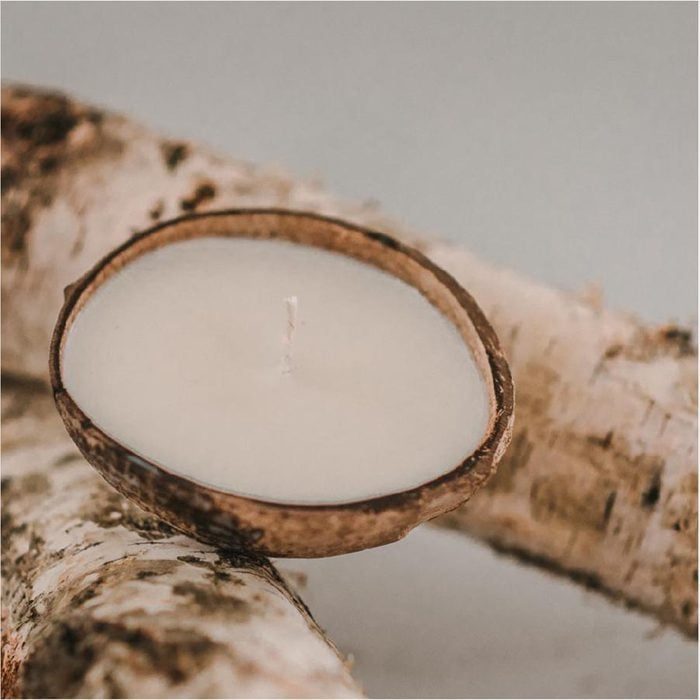 Coconut candle rests unlit on textured wood, set against a neutral background.
