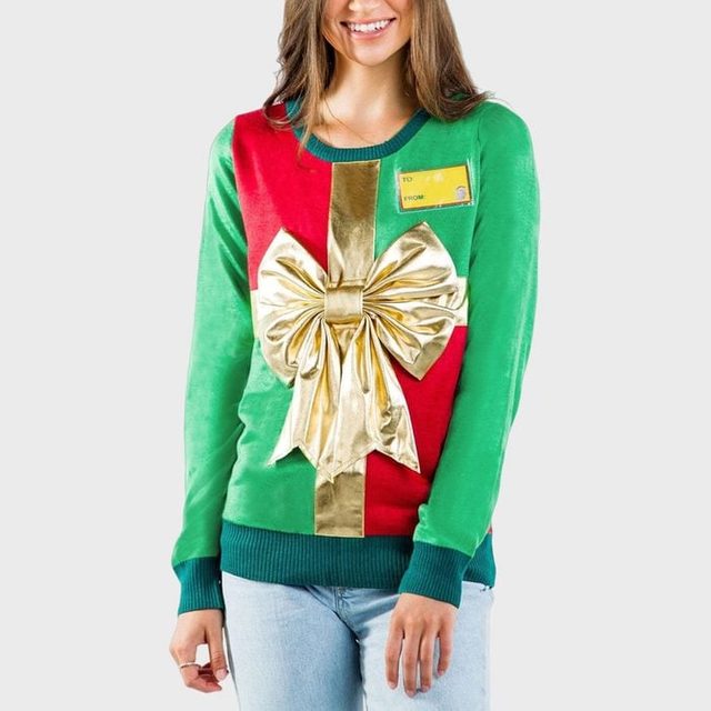 A festive sweater displays a large gold bow and gift tag design; worn by a person against a plain background.