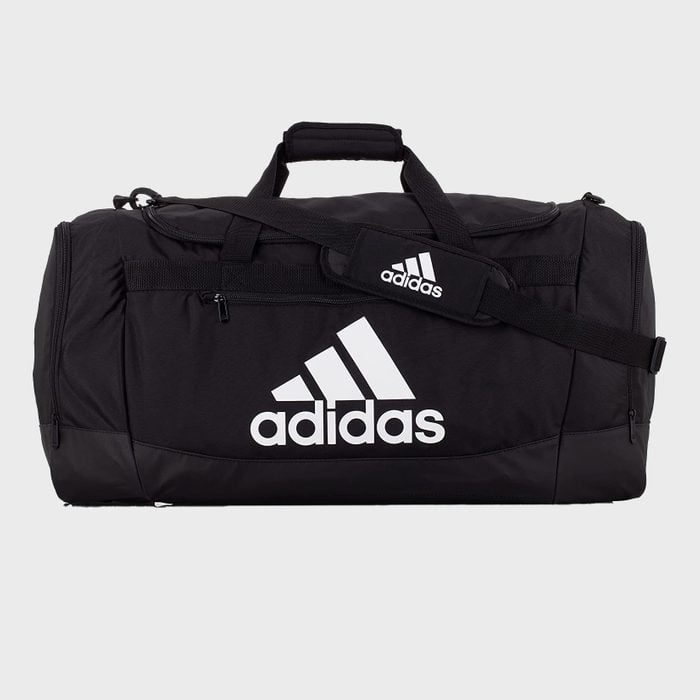 Black duffel bag, displaying the Adidas logo, lying against a plain background with handles and a shoulder strap.