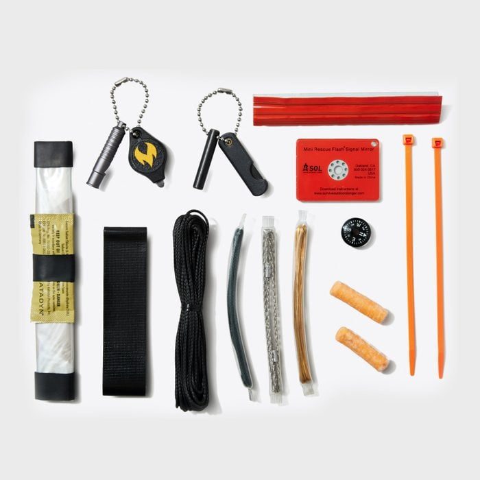 Survival kit featuring tools arranged on a white surface, including a flashlight, compass, signal mirror, cords, and adhesive bandages.
