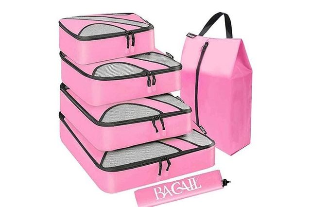 Pink packing cubes stack neatly; adjacent, a matching shoe bag with a handle and zipper stands upright. Text: 