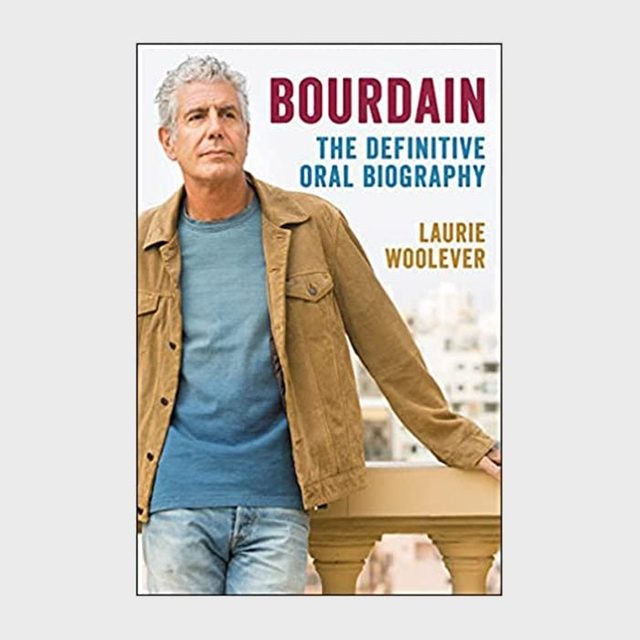 Man stands relaxed on a balcony, wearing a brown jacket and blue shirt against blurred cityscape. Text: 