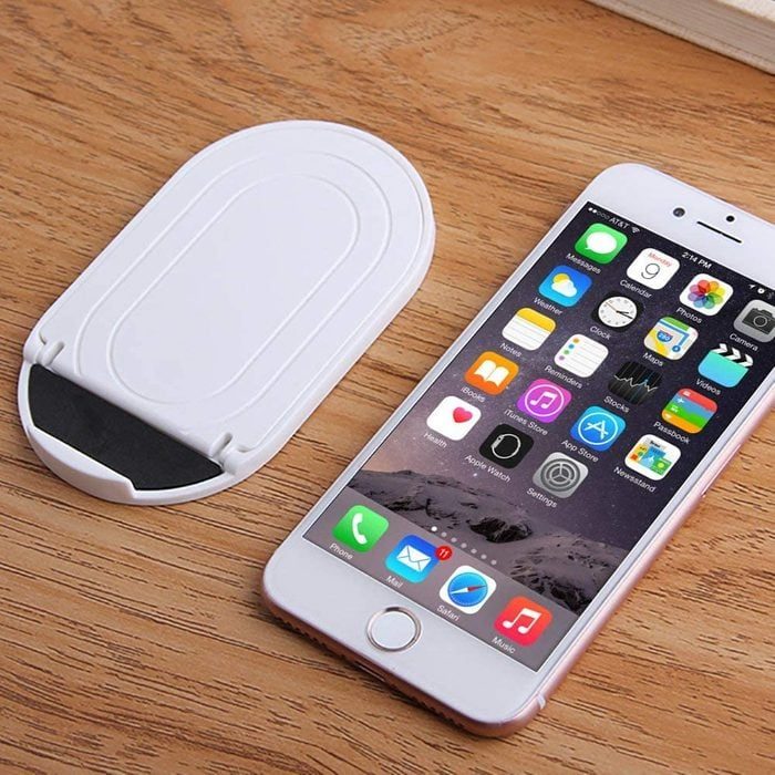 Smartphone displaying app icons lying next to a white stand on a wooden surface.